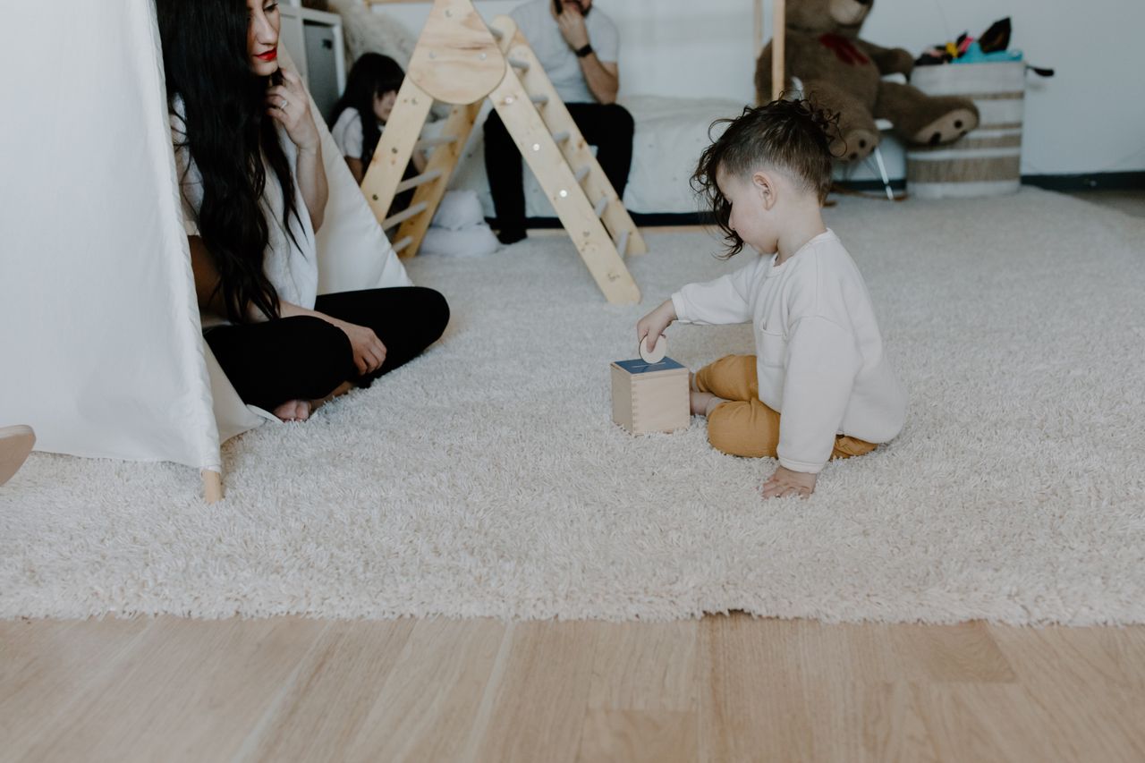 About A mother and child enjoying playtime on a carpeted floor with toys.